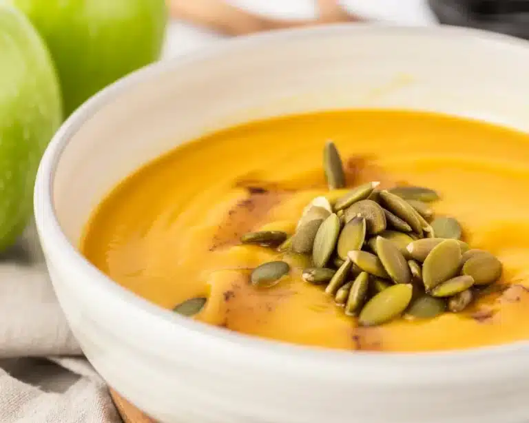 Creamy butternut squash apple soup garnished with fresh herbs and spices.