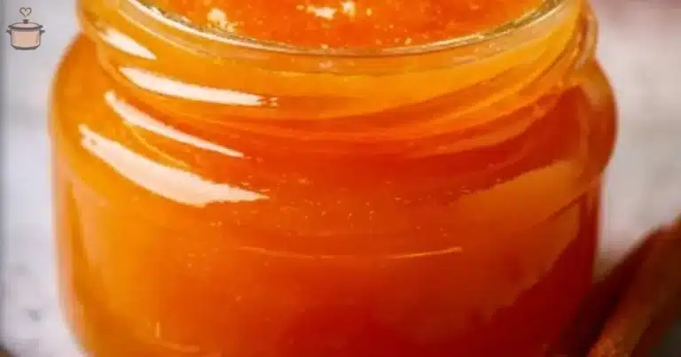 A jar of homemade orange jam with fresh oranges on a wooden table
